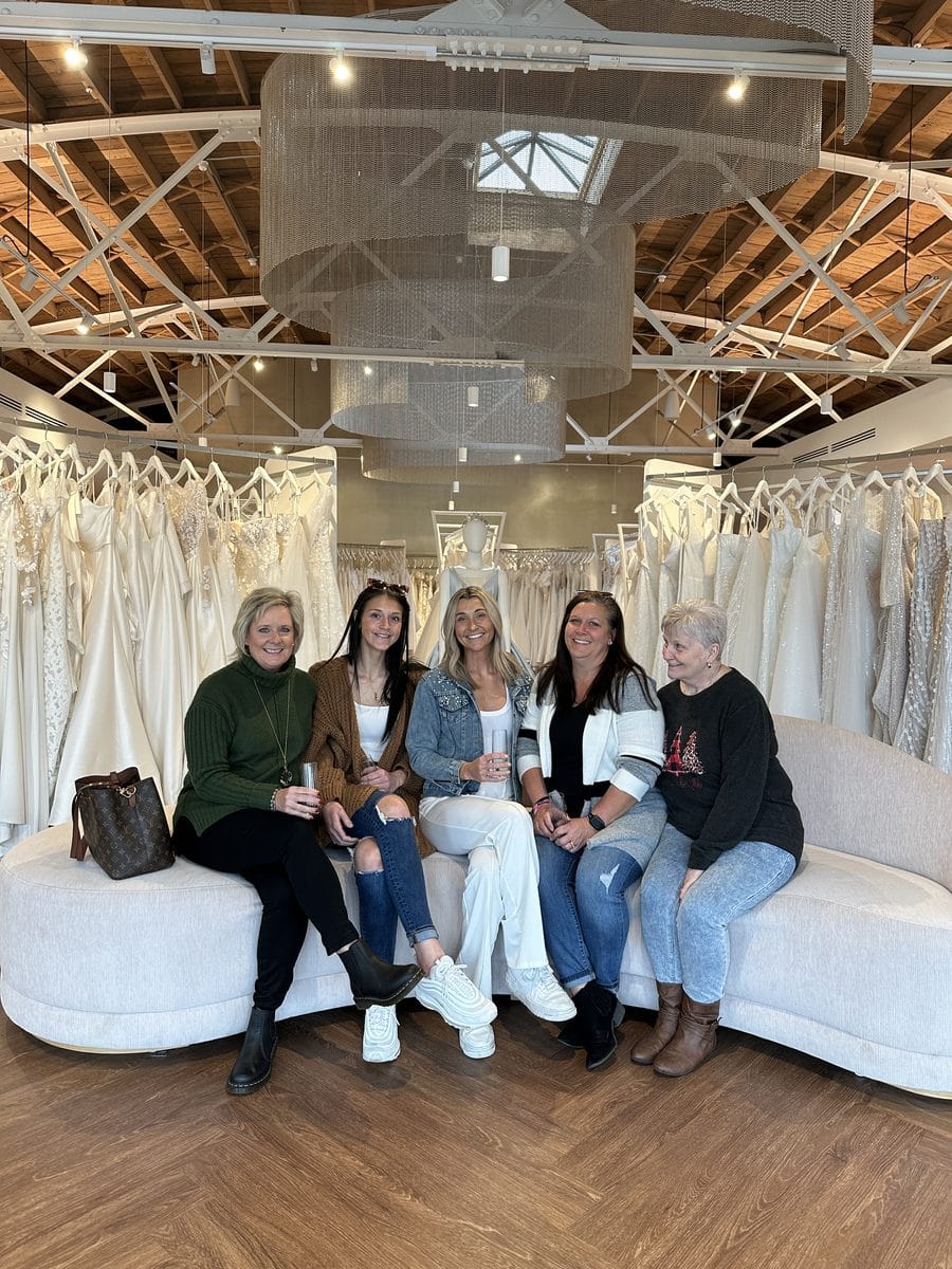 a bride and 4 of her family members sitting on a couch under our chandelier at the front of our boutique with wedding dresses in the back